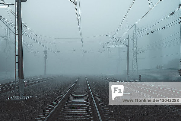 Eisenbahnschienen durch Strommasten in der Stadt bei nebligem Wetter