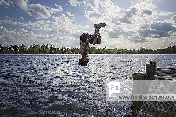 Junge ohne Hemd springt bei bewölktem Himmel in den See