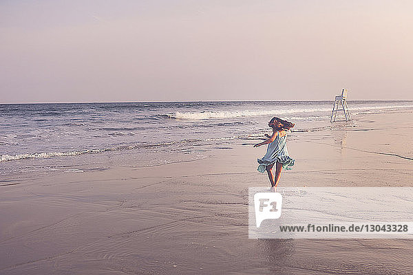 Rückansicht eines glücklichen Mädchens  das bei Sonnenuntergang am Strand gegen den Himmel spielt
