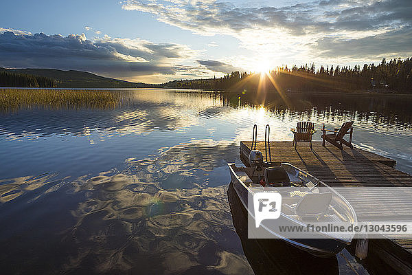Boot am Holzpier am See vor bewölktem Himmel bei Sonnenuntergang vertäut