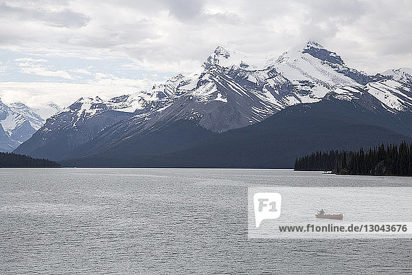 High angle view of person sailing in boat on Maligne Lake by snowcapped mountains against cloudy sky at Jasper National Park
