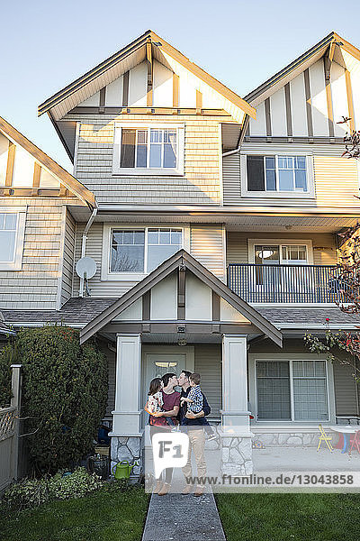 Paar mit Kindern  die sich küssen  während sie vor dem Haus stehen