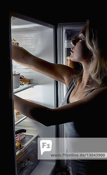 Nahaufnahme einer Teenagerin  die in der Küche Lebensmittel aus dem Kühlschrank nimmt