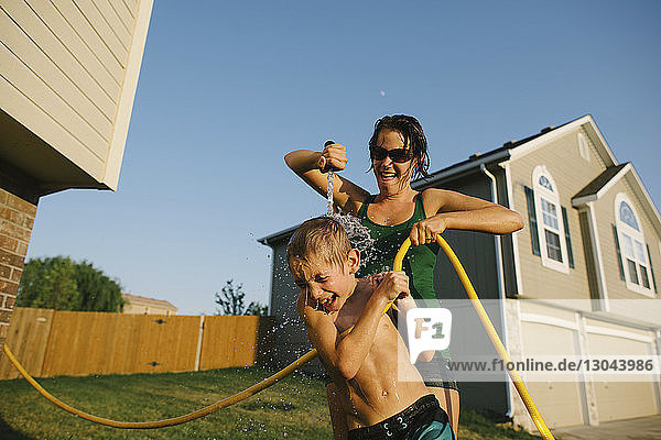 Playful mother pouring water on son using hose pipe in yard