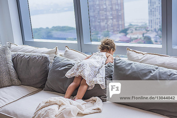 Girl looking through window while lying on pillows at home