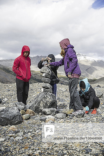 Siblings stacking rocks on mountain against cloudy sky at Jasper National Park