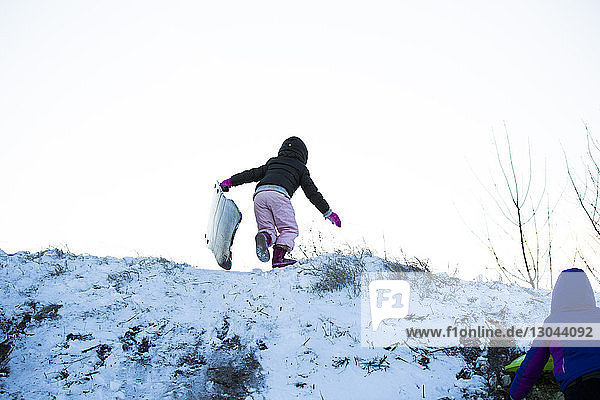 Low angle view of sisters climbing snow covered hill against clear sky