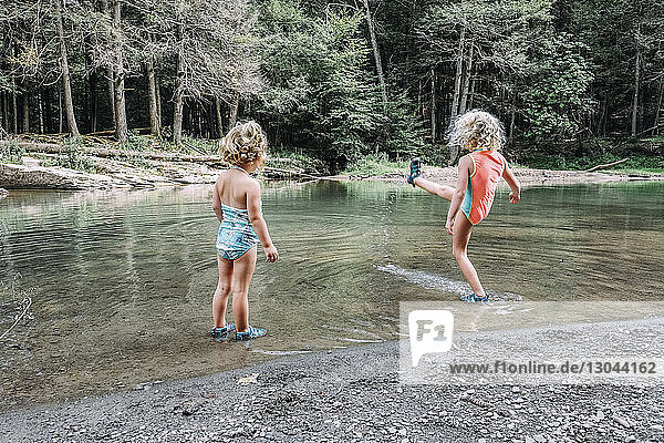 Rückansicht eines Mädchens  das seine Schwester im See stehend beim Wassertreten beobachtet