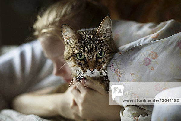 Frau umarmt Katze  während sie zu Hause auf dem Bett liegt