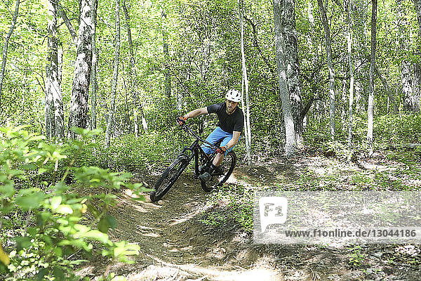 Confident man mountain biking on dirt road at forest