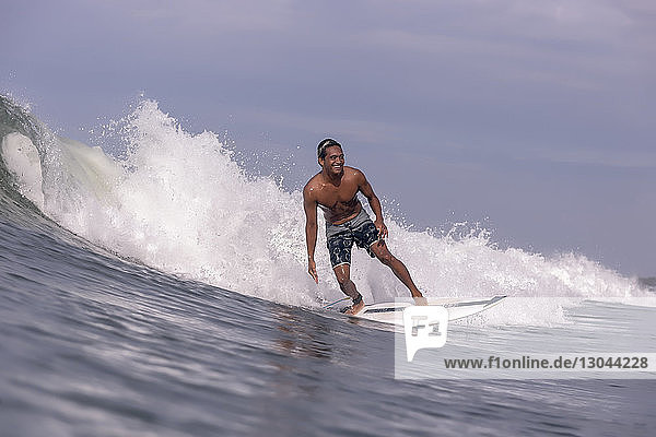 Shirtless man surfing on sea against sky