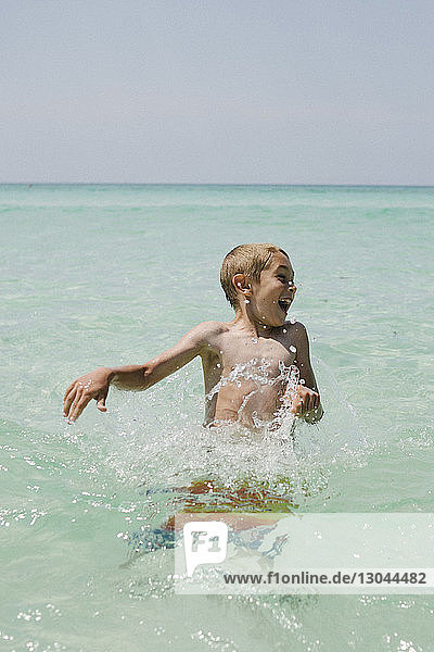 Happy boy playing in sea against clear sky