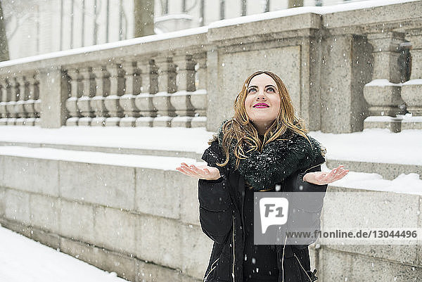 Smiling woman enjoying snowing while standing against building in city