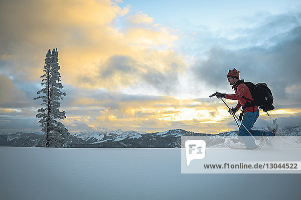 Side view of male hiker skiing on snowy field during sunset
