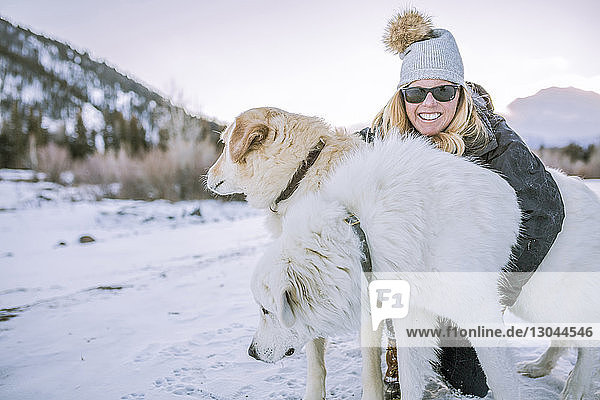 Happy woman embracing dogs on snowy field during sunset