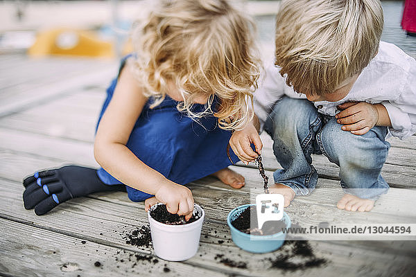 Friends playing with earthworms in dirt while crouching on jetty