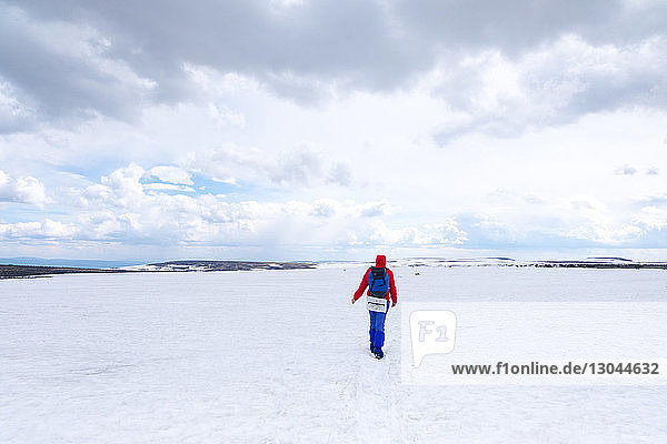 Rear view of hiker walking on snow covered field against cloudy sky