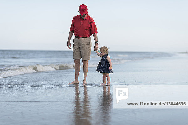 Großvater mit Enkelin am Strand gegen den Himmel stehend