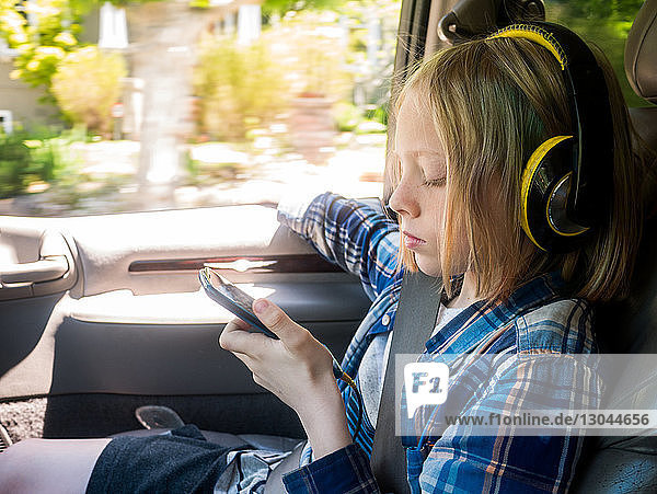 Boy looking at mobile phone while listening music in car