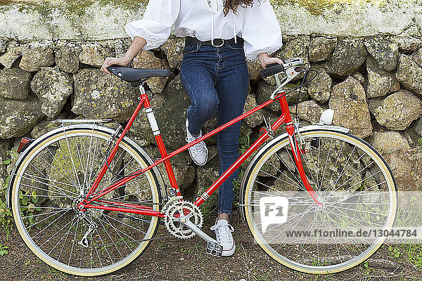 Niedriger Teil einer Frau mit Fahrrad an einer Steinmauer stehend