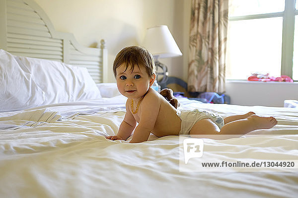 Porträt eines süßen hemdlosen Kleinkindes  das zu Hause auf dem Bett liegt