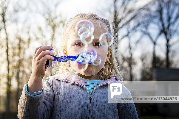 Portrait of girl blowing bubbles at backyard