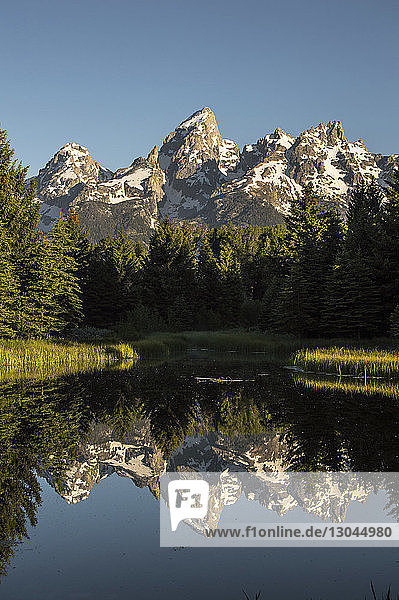 Snow covered mountain against clear sky reflecting on calm lake at Grand Teton National Park