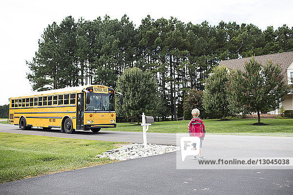 Rückansicht eines Jungen mit Rucksack  der auf den Schulbus wartet