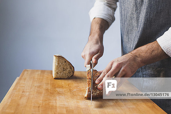 Ein Mann schneidet in der Küche einen Brotlaib in der Mitte