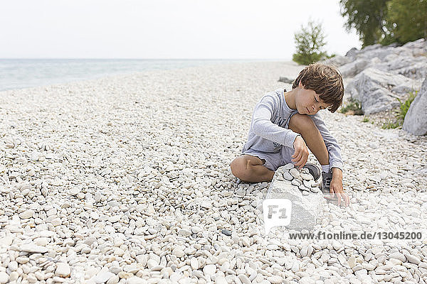 Sorgenfreier Junge spielt mit Kieselsteinen am Seeufer