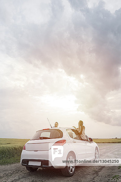 Auf Autoscheiben sitzendes Ehepaar auf einem Feld vor bewölktem Himmel