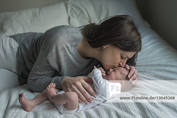 High angle view of mother kissing crying newborn baby boy on forehead in bed