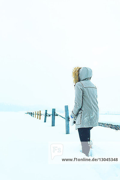 Rückansicht einer Frau  die an einem Geländer auf einem schneebedeckten Feld steht