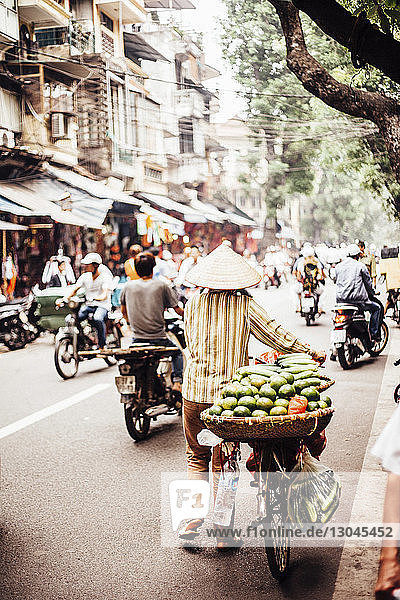 Rückansicht eines Mannes  der auf einem Fahrrad auf dem Markt Obst und Gemüse in einem Korb trägt