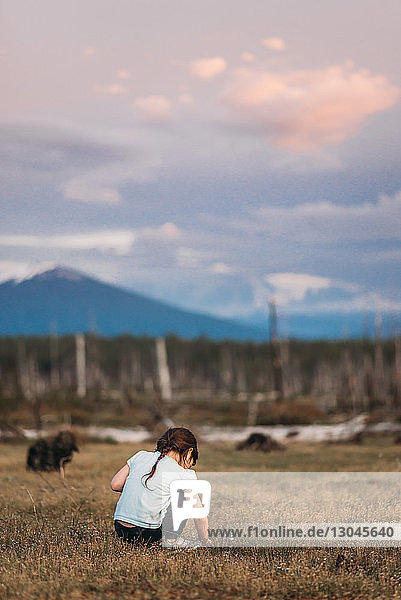 Rear view of girl crouching on field against sky