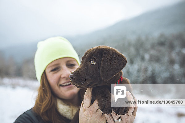 Glückliche Frau mit Schoko-Labrador steht im Winter auf dem Feld