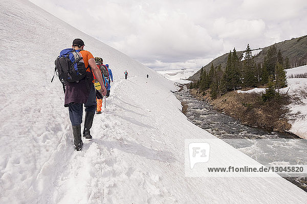 Rückansicht von Wanderern  die auf einem schneebedeckten Hügel vor bewölktem Himmel gehen
