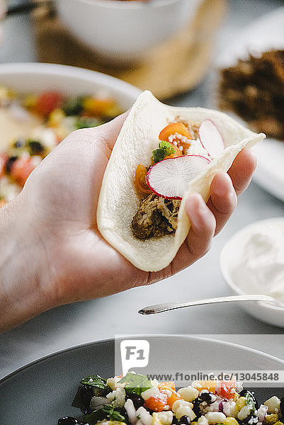 Abgehackte Hand eines Mannes  der Tacos am Esstisch hält