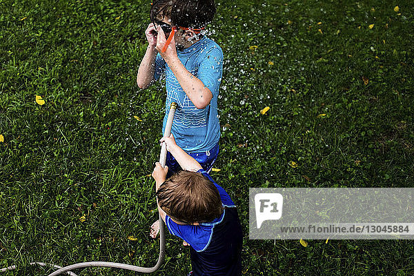 High angle view of brothers playing with garden hose in yard