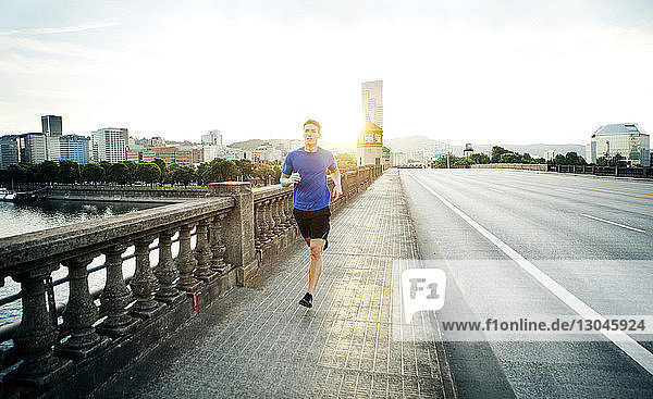 Sportlicher Mann joggt auf Fußweg gegen den Himmel in der Stadt