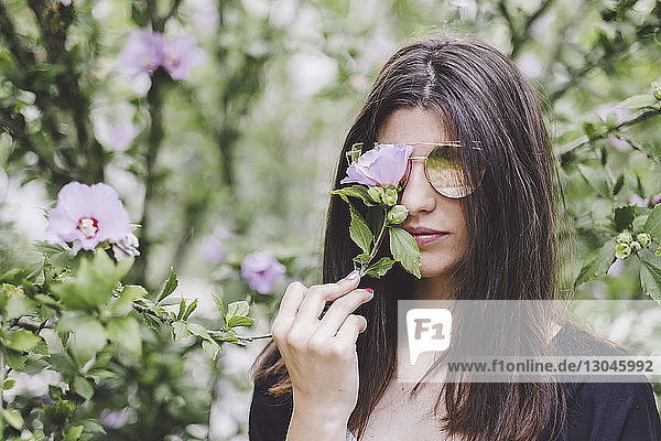 Porträt einer Frau mit Sonnenbrille  die im Park Blumen hält