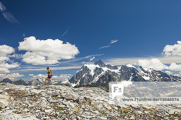 Mid distance view of female backpacker hiking against mountains and sky during winter at North Cascades National Park