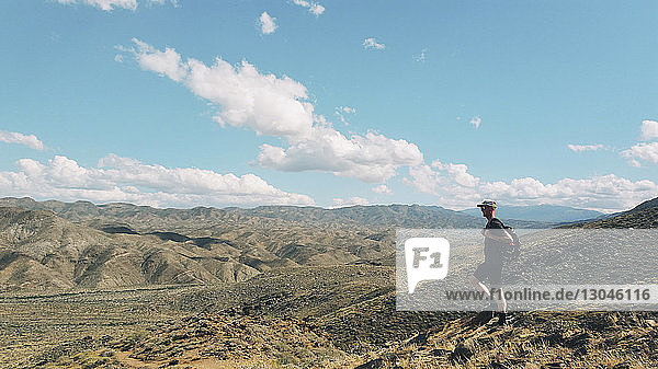 Männlicher Wanderer mit Rucksack  der am sonnigen Tag auf dem Feld gegen den Himmel läuft