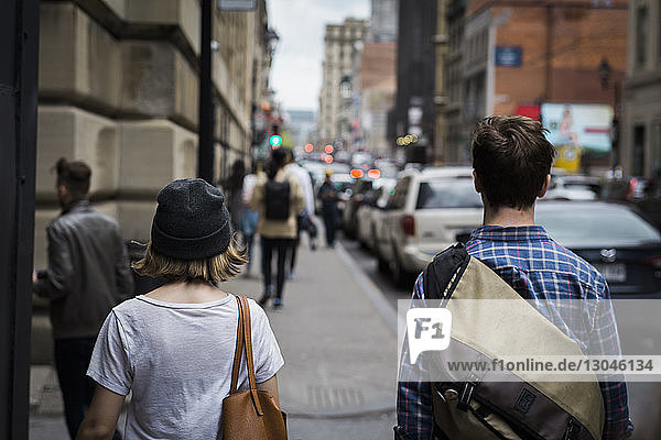 Rear view of friends walking on sidewalk in city