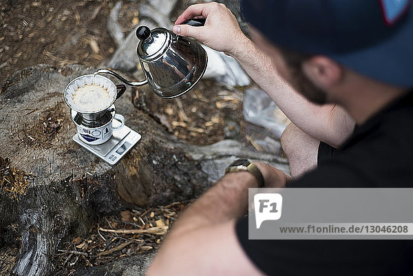 Schrägaufnahme eines Mannes  der auf dem Campingplatz Kaffee in den Filter gießt