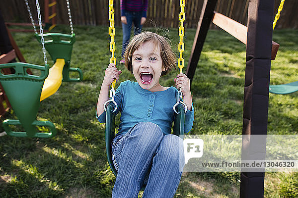 Portrait of happy girl swinging at playground with mother in background