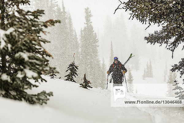 Mann mit Skiern geht auf schneebedecktem Feld