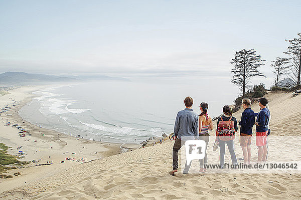 Freunde stehen zusammen auf Sand am Strand gegen den Himmel