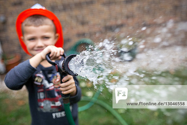 Boy wearing helmet while spraying water with garden hose at backyard