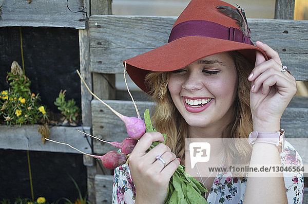 Fröhliche junge Frau hält Hut  während sie Radieschen betrachtet